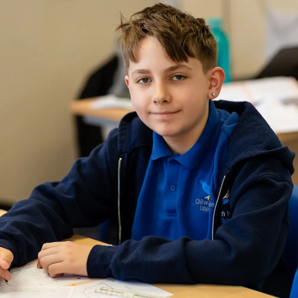 Male pupil with brown hair at Chilworth House School working in a classroom smiling at the camera