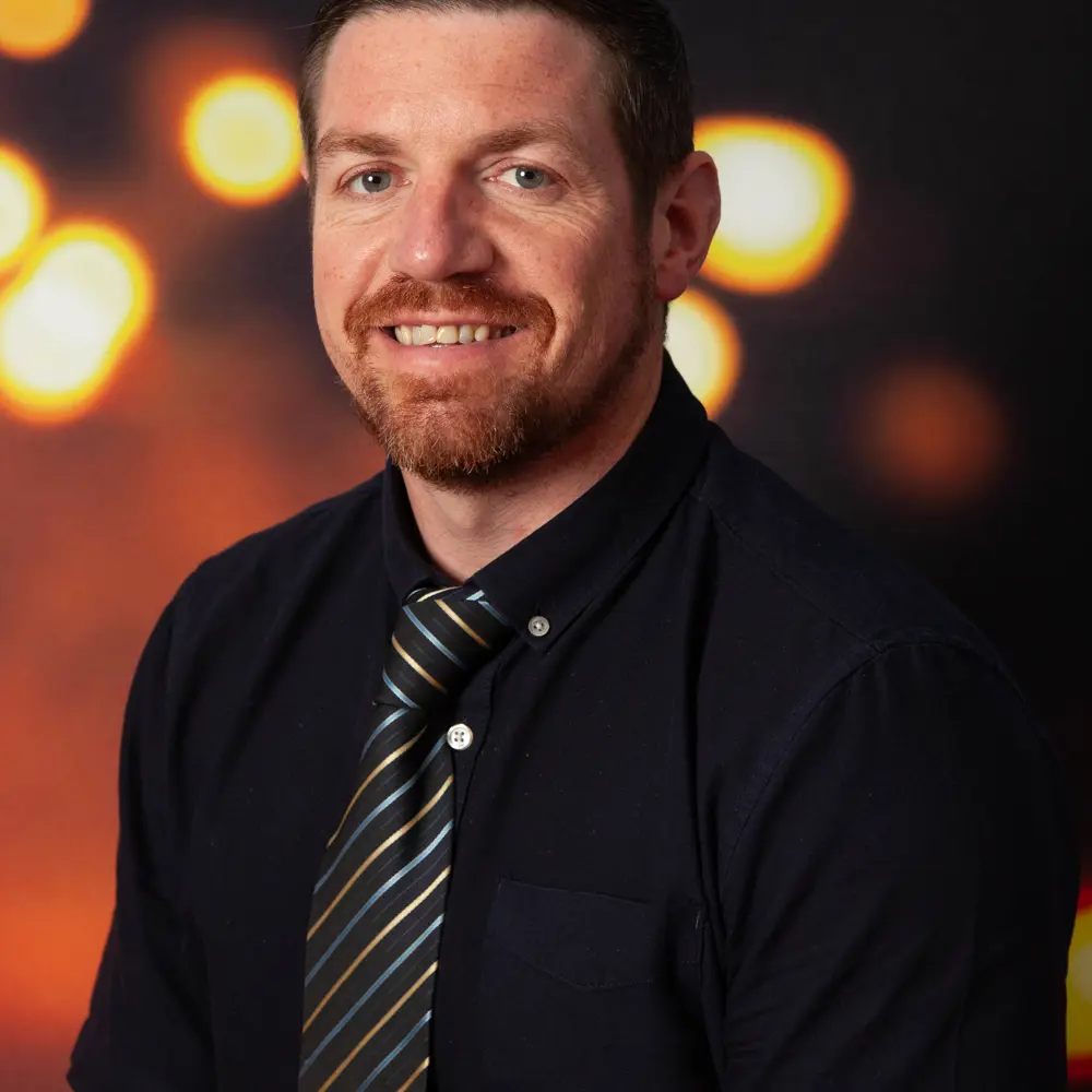 A portrait photograph of Neil Bourke smiling at the camera wearing a shirt and tie