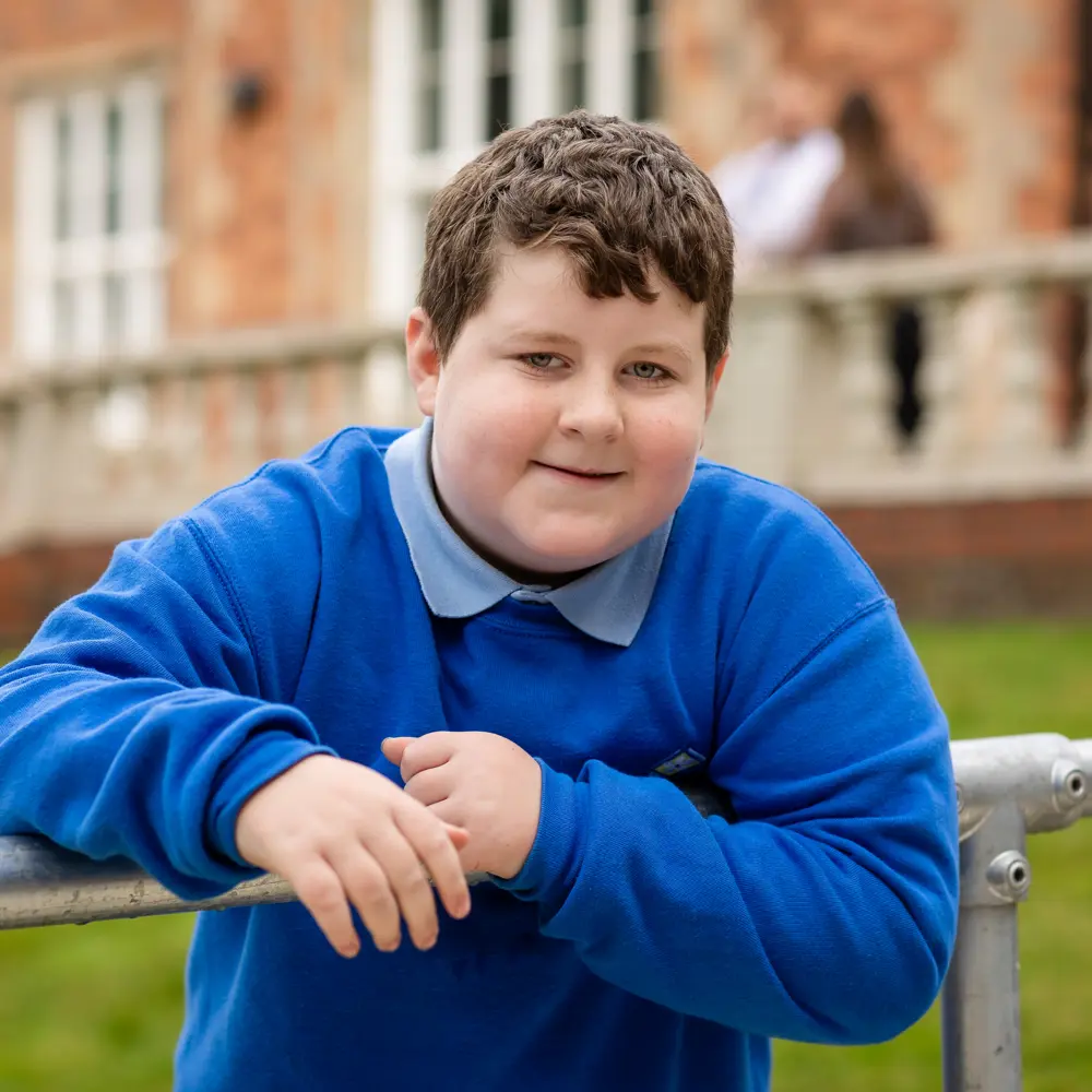 Young boy from Hinckley House School leaning against metal rails smiling into camera