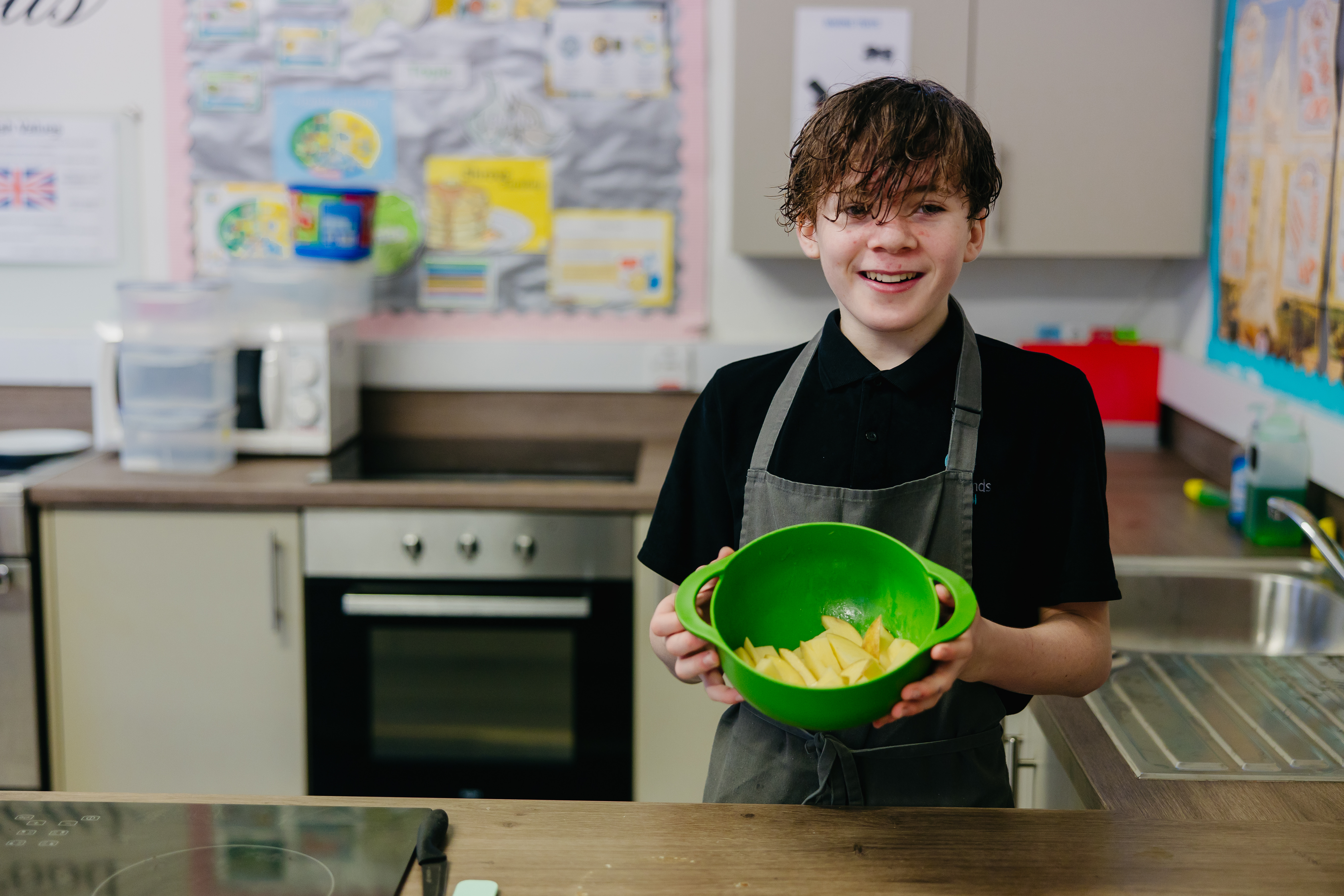 Pupil in school kitchen wearing apron holding bowl of ingredients