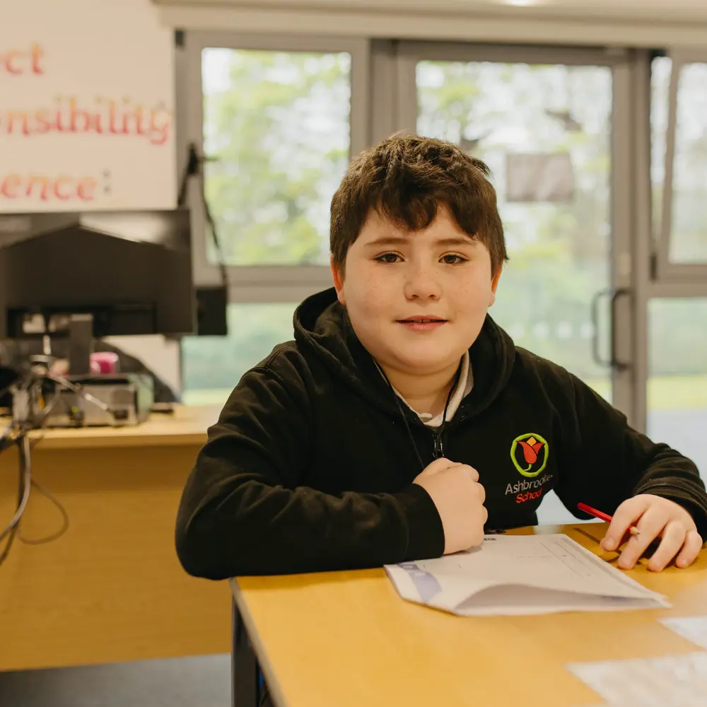 Young dark-haired boy sat at his desk completing classwork in a classroom at Ashbrooke School