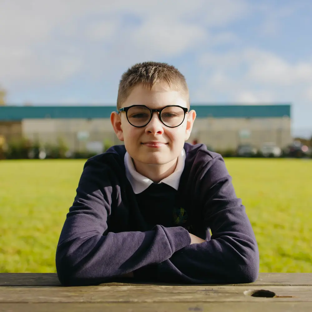 Young boy from Millcourt School sat on a bench with his arms crossed smiling into camera