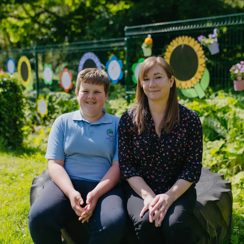 Pupil and teacher sat together on a tractor tyre in the school playground