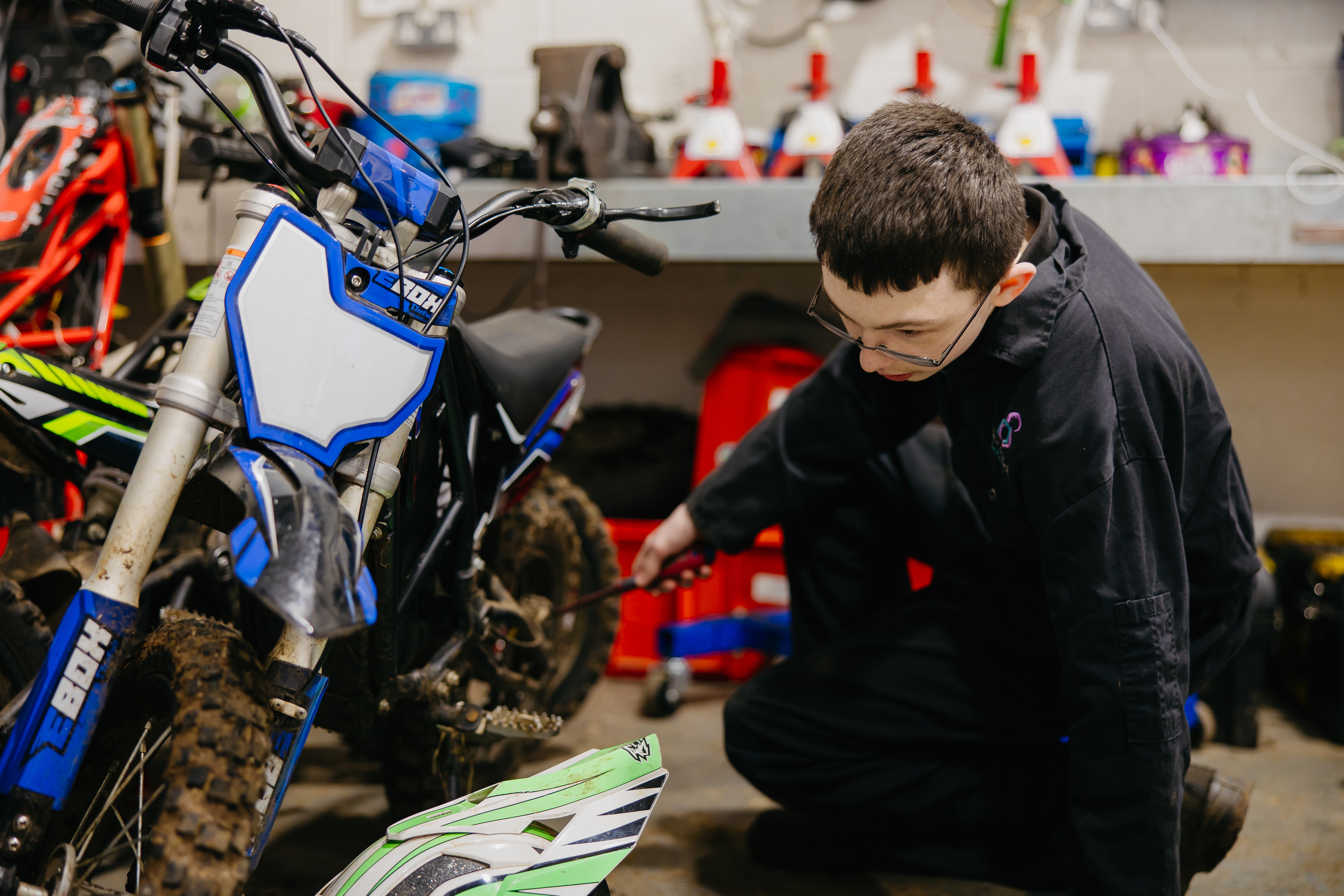Boy wearing navy overalls assessing a bike in a motor vehicle workshop