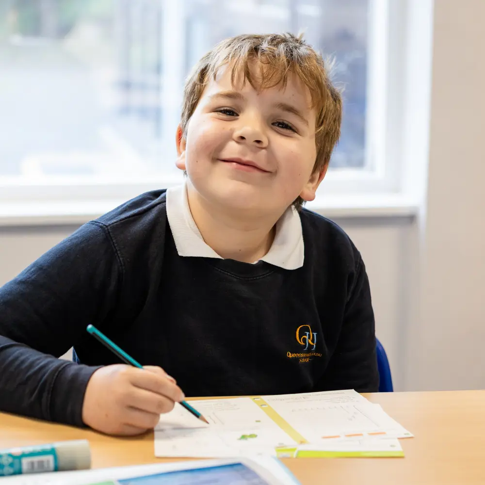 A young boy from Queensmead House School working in a classroom smiling at a camera