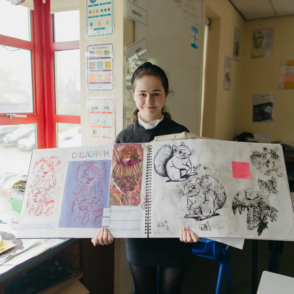 Young girl showing her artwork in a classroom at Ashbrooke School