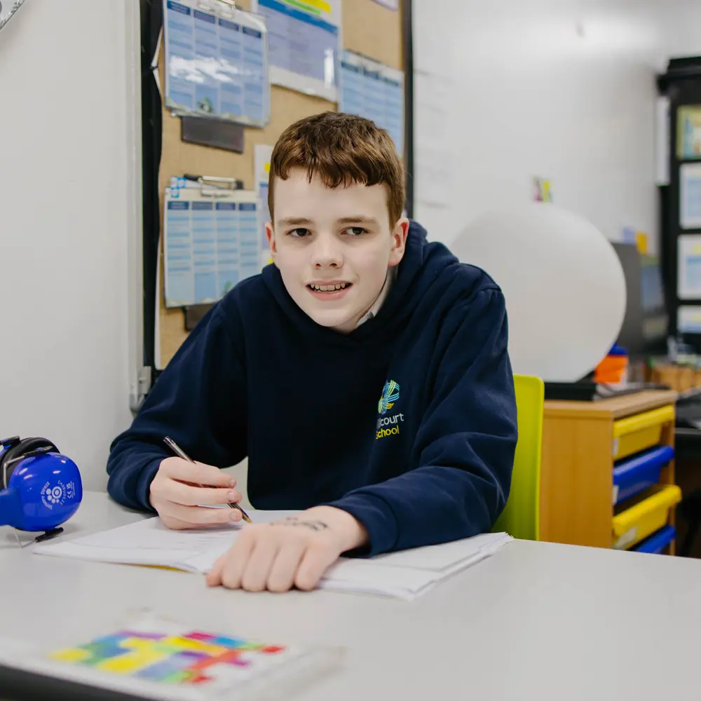 A young boy with brown hair from Millcourt School working in a classroom wearing a blue hoodie