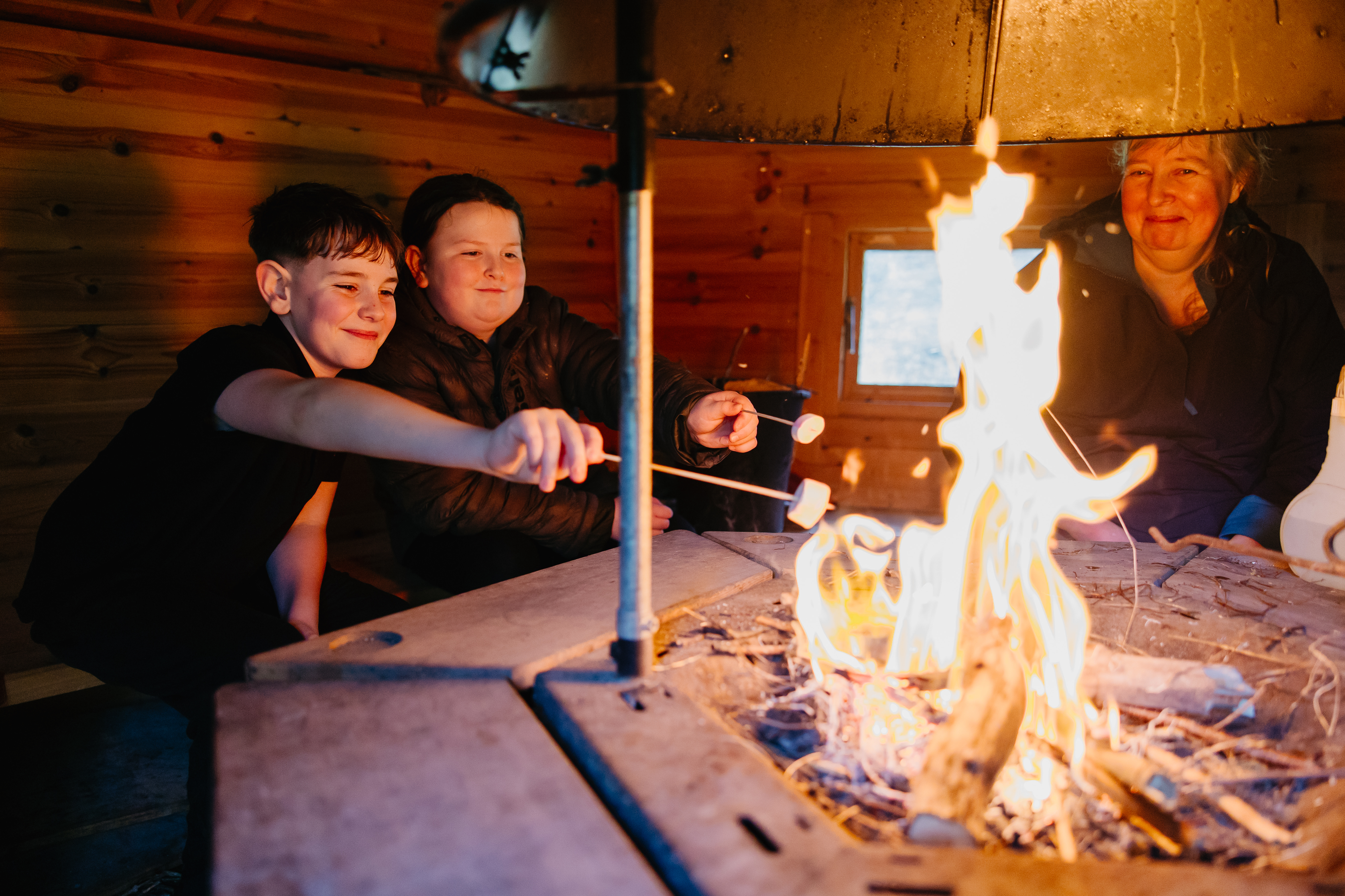 Two pupils and a staff member sat round a campfire toasting marshmallows