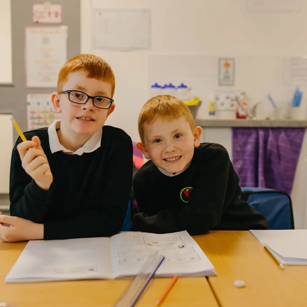 Two young boys sat next to each other completing classwork at Ashbrooke School
