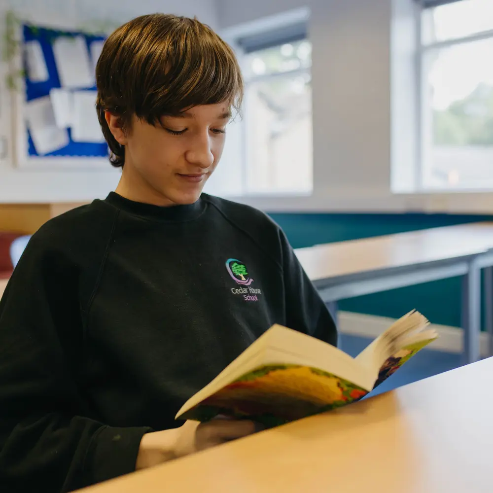 Boy from Cedar house School sat at a desk in a classroom reading