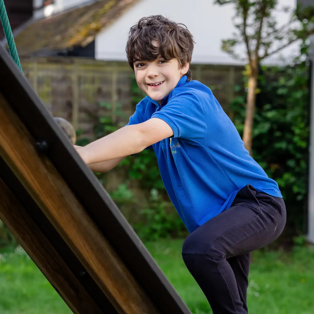 Male pupil with dark brown hair at Bramley Hill School climbing in the play ground