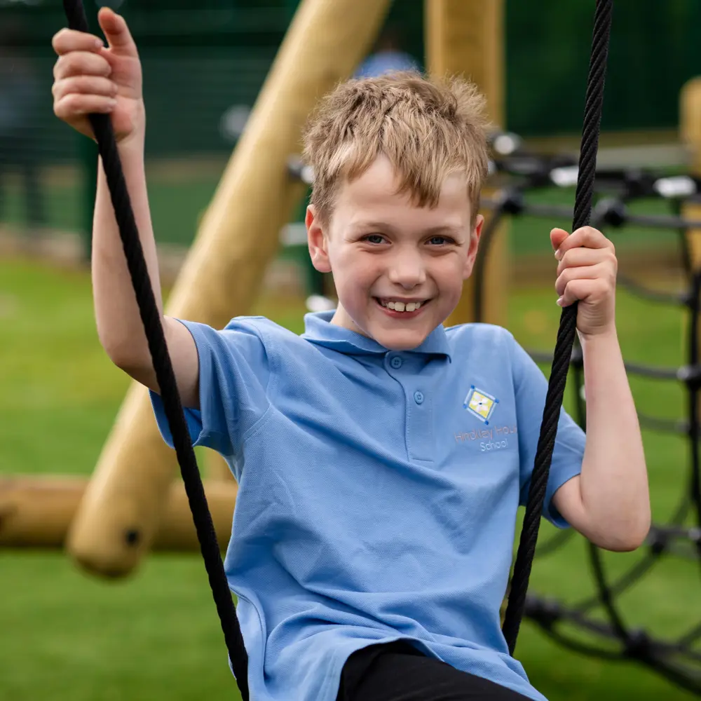 Young boy with blonde hair from Hinckley House School playing on climbing frame and smiling at the camera