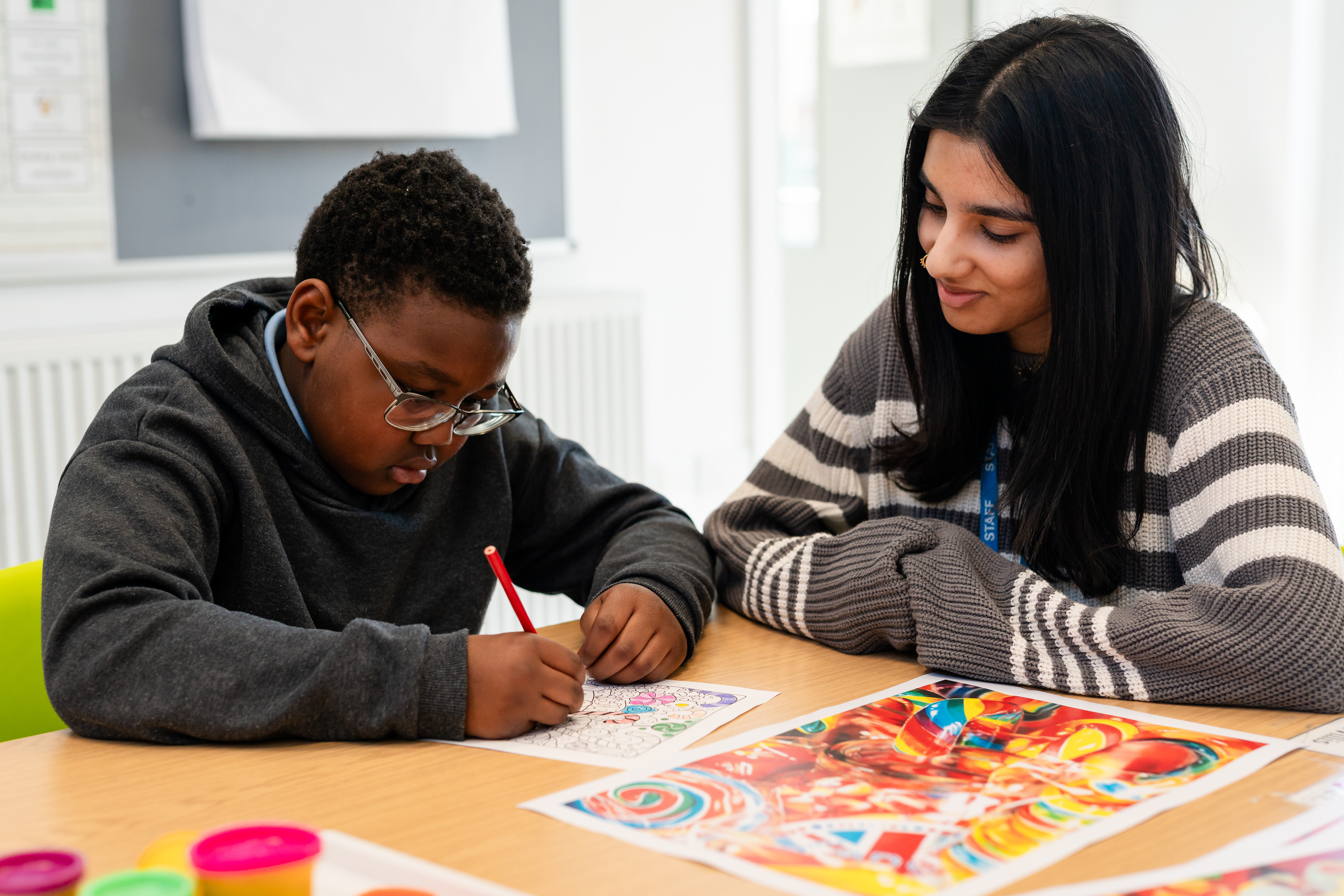 Staff memeber sat with pupil as he does colouring in