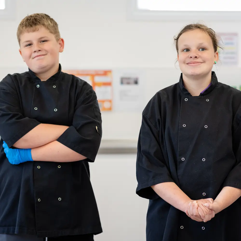 A young boy and girl at Bramley Hill School wearing black cooking aprons in class