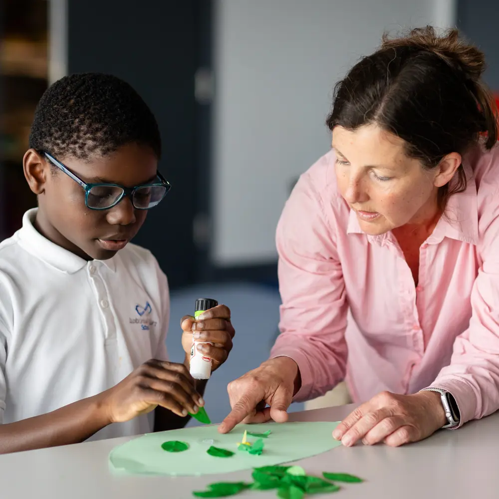 Young boy and teacher from Luxborough Court School using a glue stick to create a leaf in a classroom