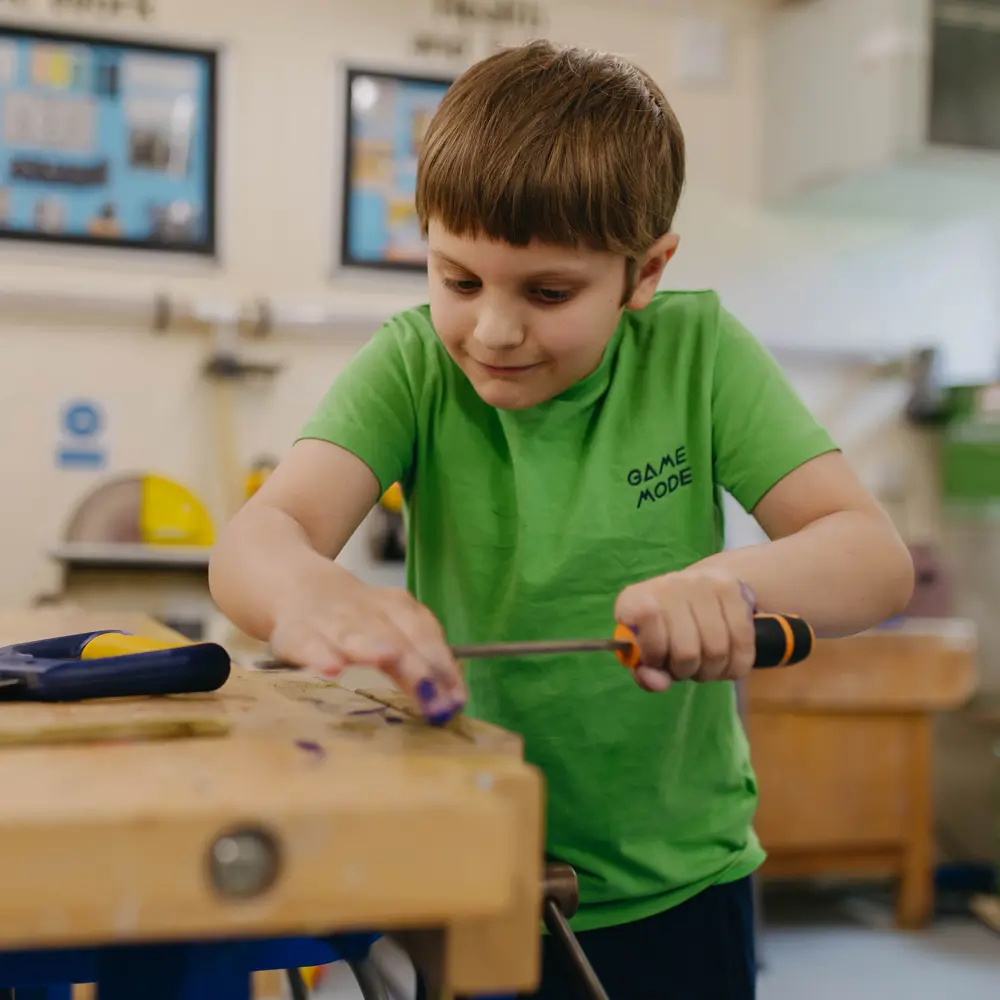 Young boy wearing a green t-shirt holding a screwdriver in the construction room at Abbeywood School