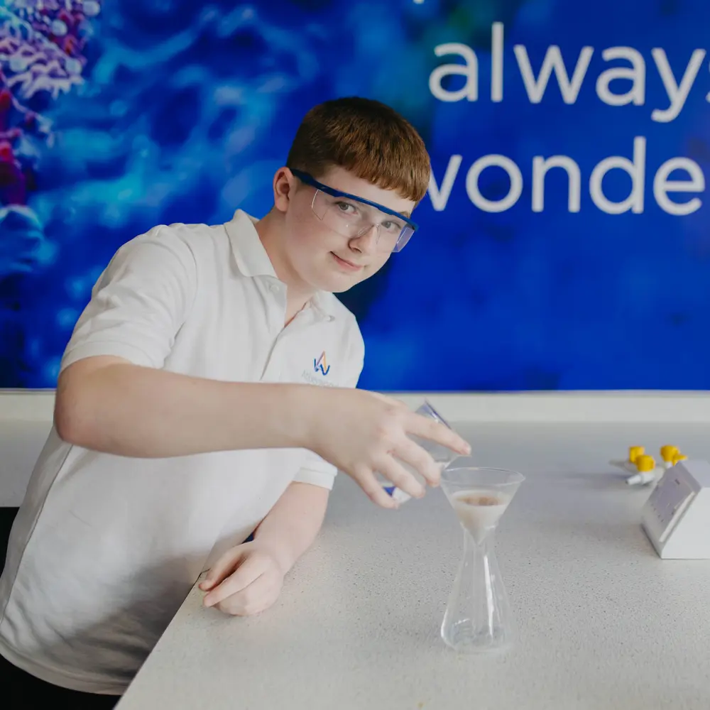 Boy wearing science safety goggles pouring liquid in the lab at Abbeywood School