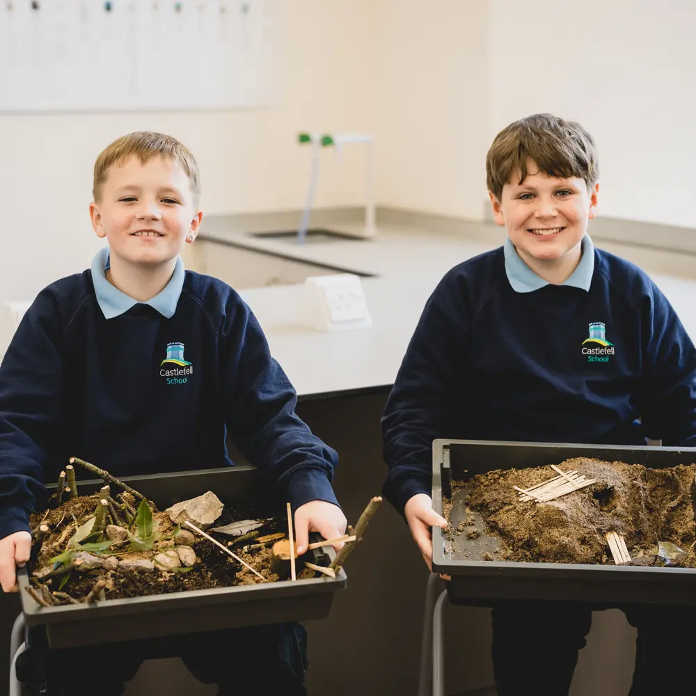 Two boys from Castlefell School in a science lesson holding trays of habitats they have made