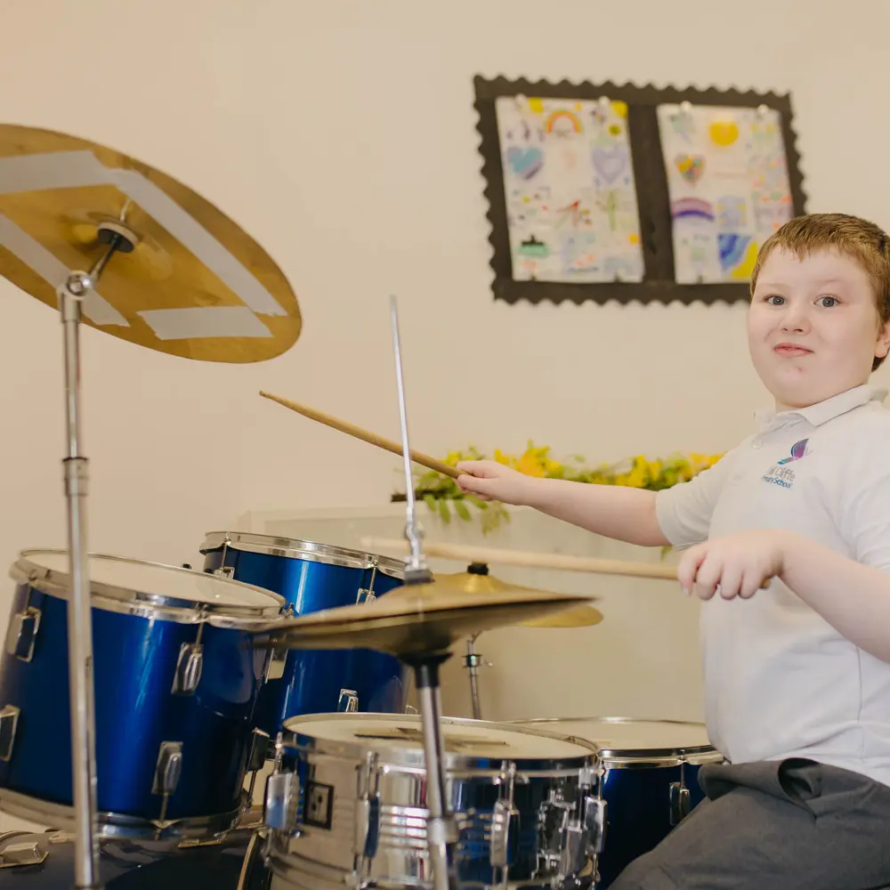 A young boy at Hall Cliffe Primary School playing the drums looking at the camera