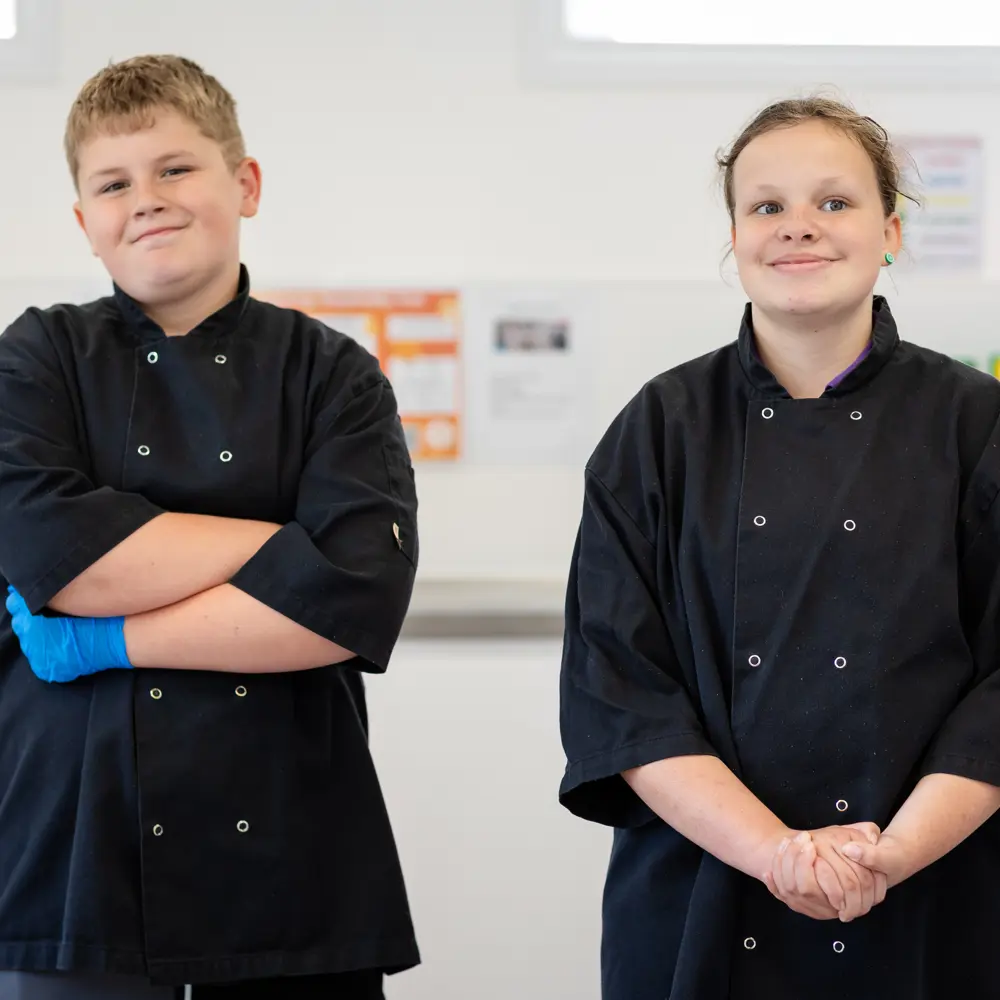 A young boy and girl at Bramley Hill School wearing black cooking aprons in class