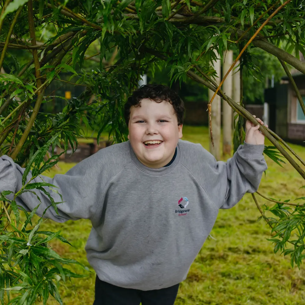 Young boy at Bridgeway School outside in the willows smiling at the camera