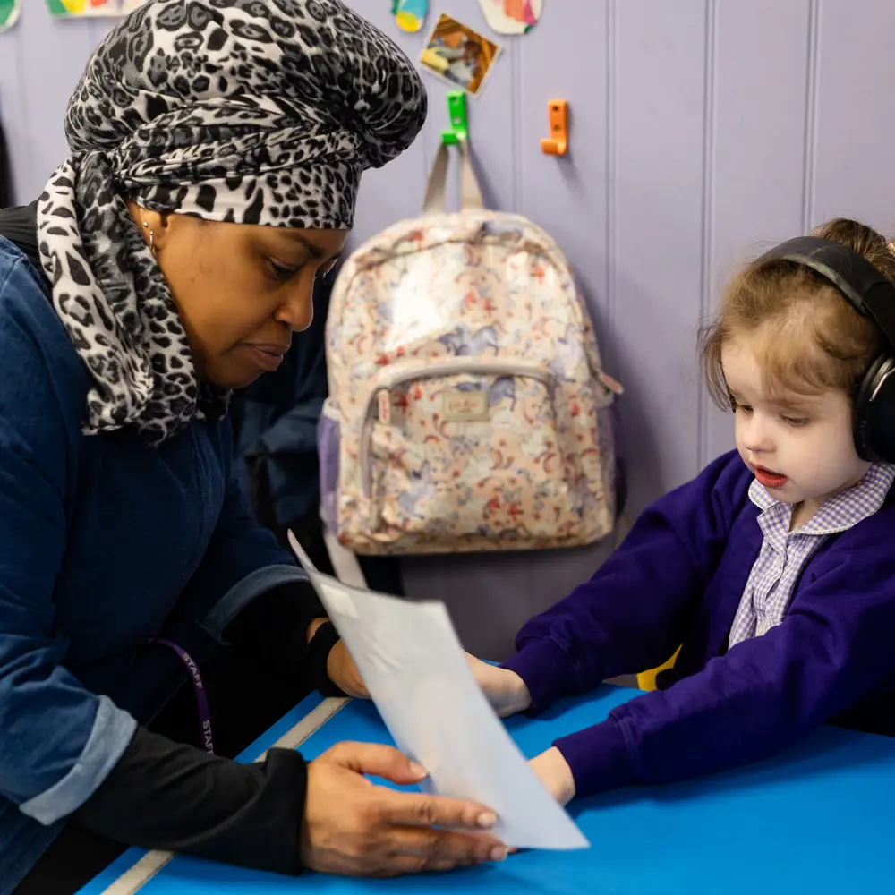 Teacher and young girl from Lavender Lodge School sat together at desk in classroom learning