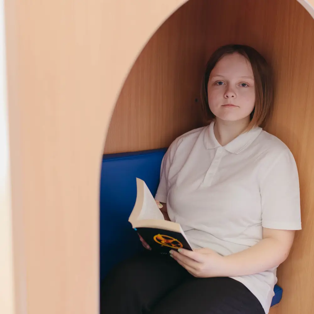 A young girl at Hartwell School sat in a reading nook reading The Hunger Games