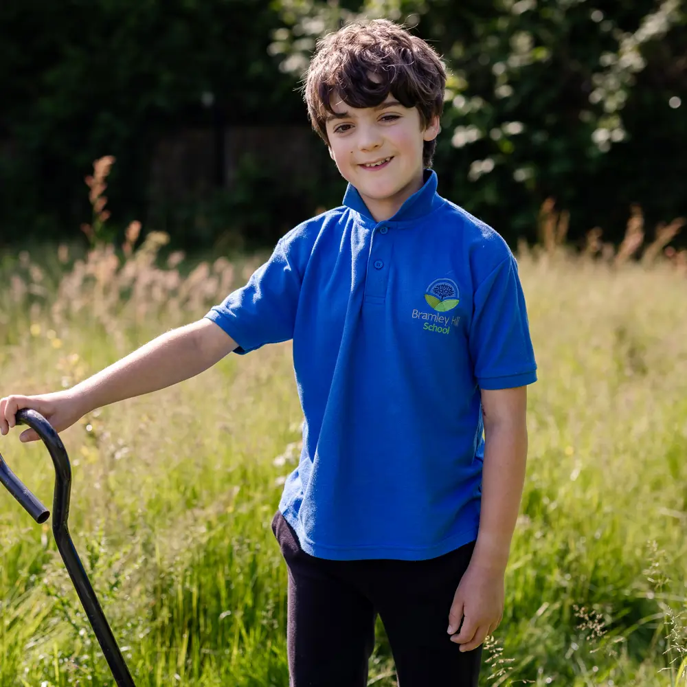 Young boy from Bramley Hill School with brown hair outside gardening wearing a blue polo shirt with school logo