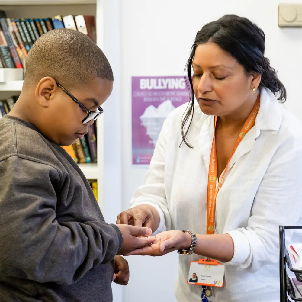 A young boy from Greenholm School being handed something by a teacher