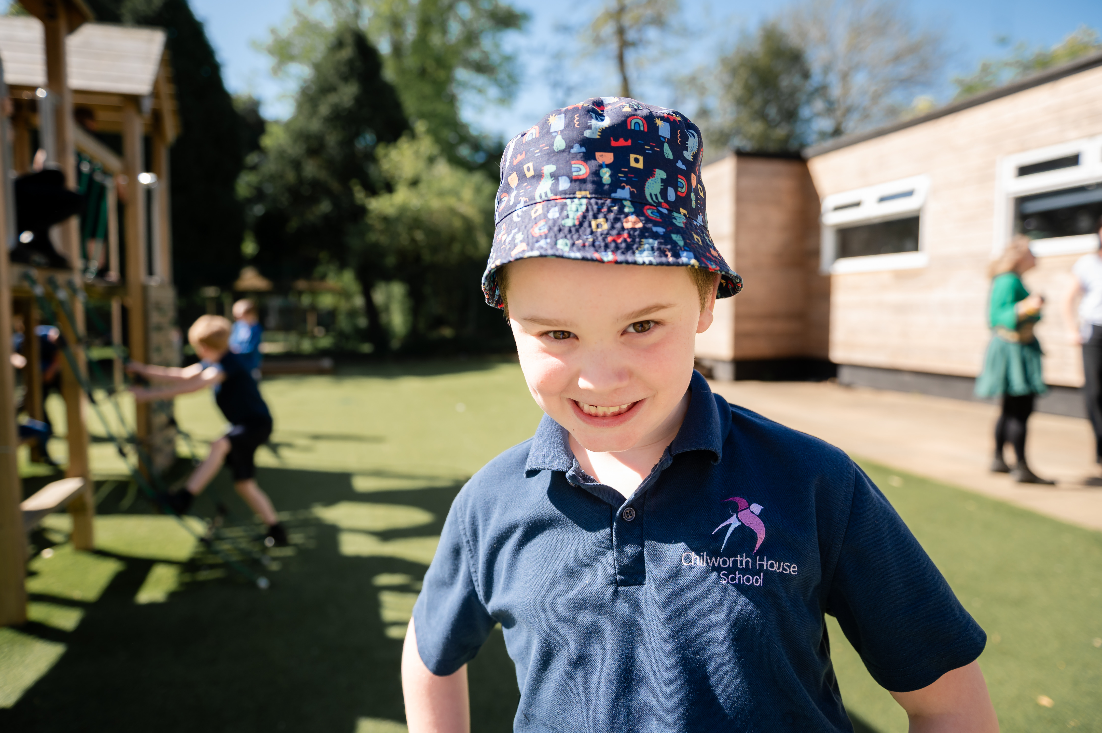 Boy wearing sun hat stood outside smiling into camera