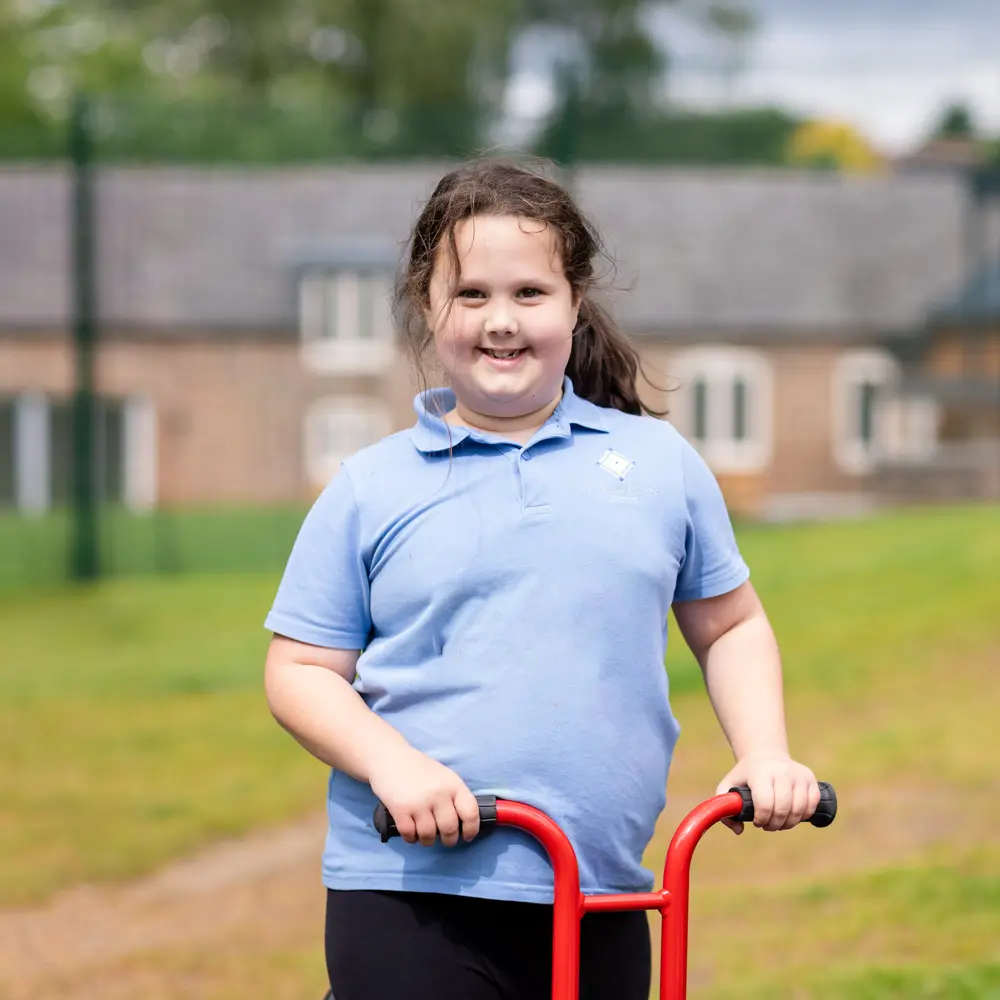 Young girl wearing blue t-shirt with brown hair smiling while riding on scooter at Hinckley House School
