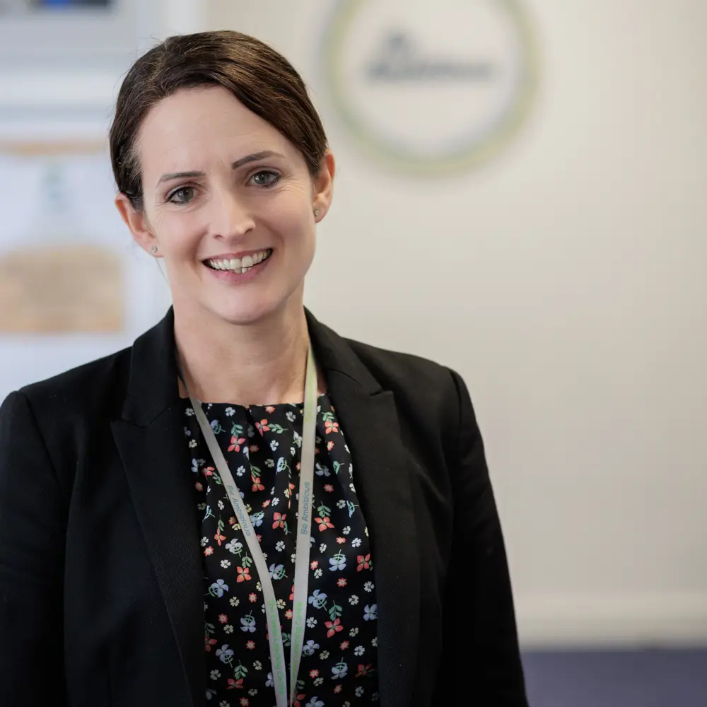 A brown haired female member of staff smiling at the camera from The Eaves Learning Centre School