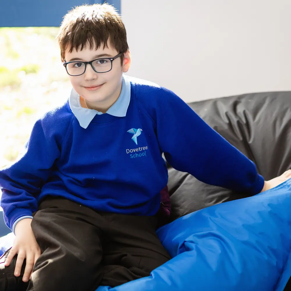 A young boy at Dovetree School sitting on a bean bag smiling at the camera