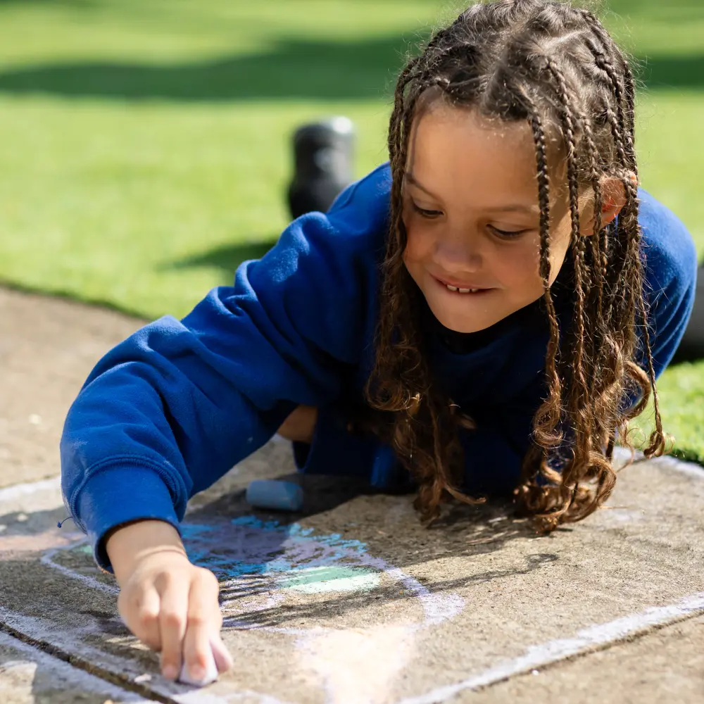 Girl from Chilworth House School lying outside playing with chalk