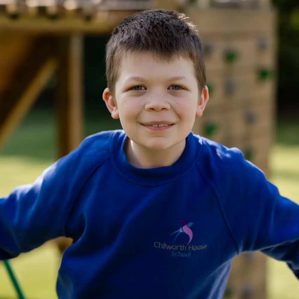 A young boy from Chilworth House School playing outside smiling at the camera