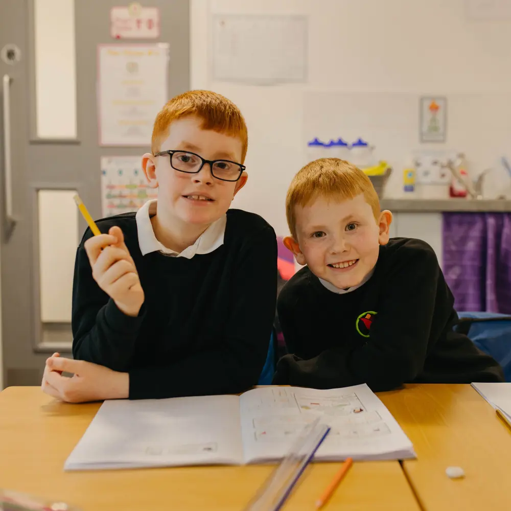 Two young boys sat next to each other completing classwork at Ashbrooke School