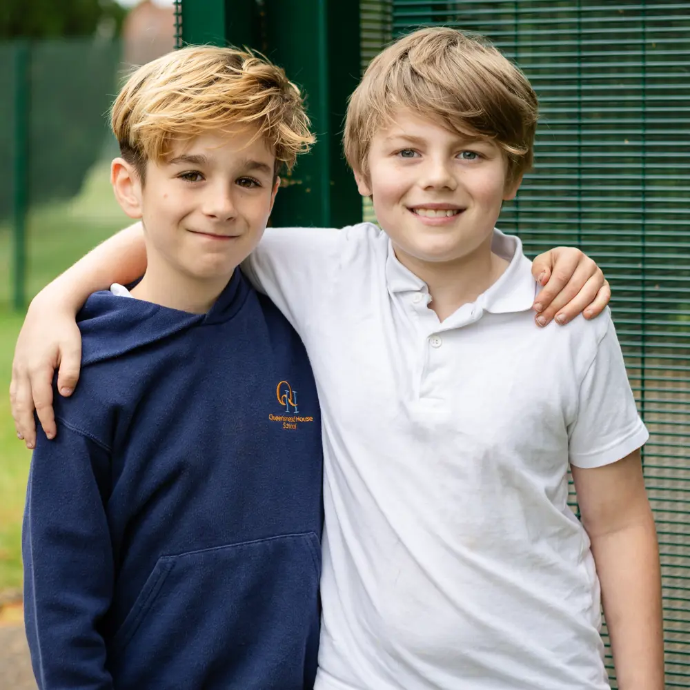 Two young boys from Queensmead House School outside with their arms round each other