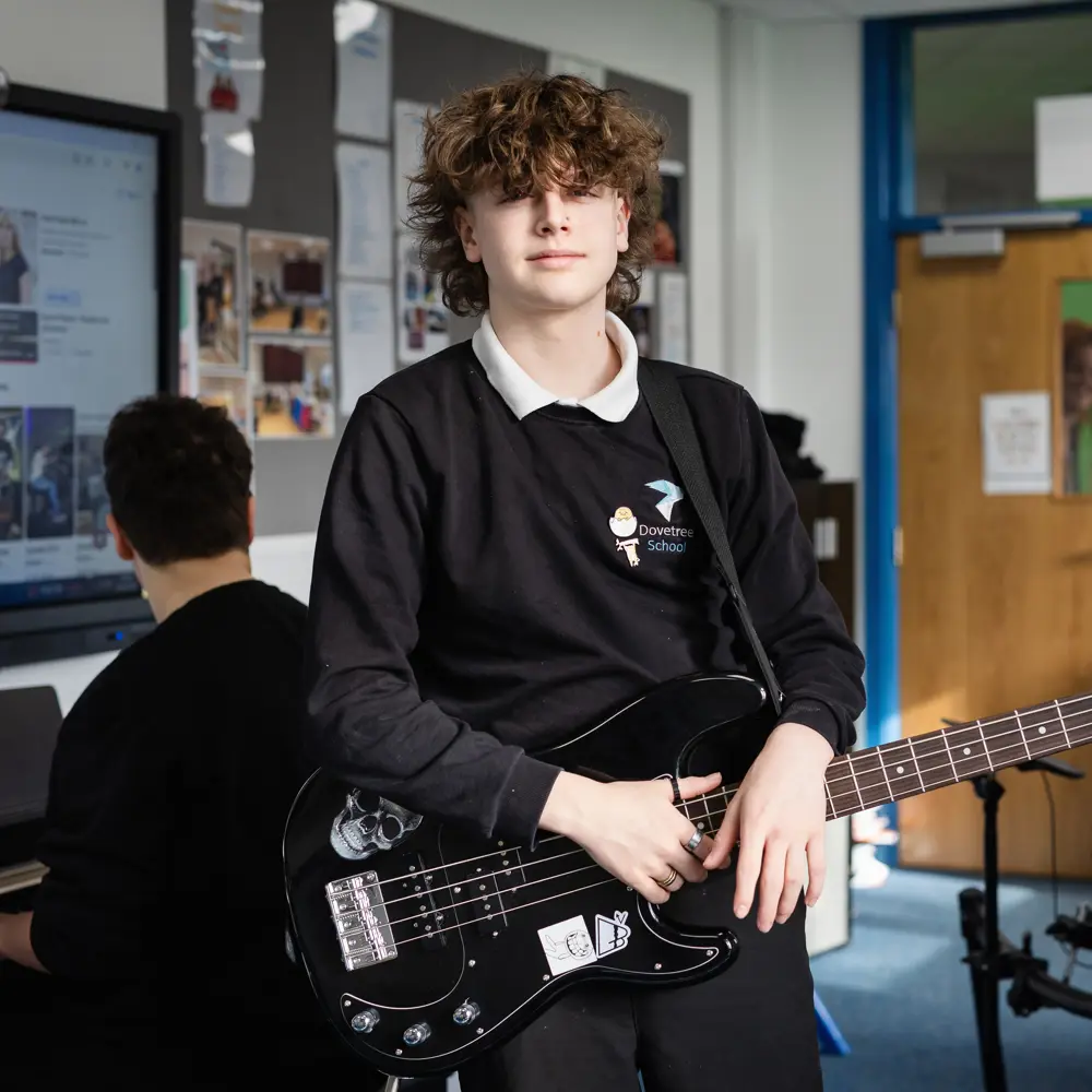 A young boy at Dovetree school playing the guitar smiling at the camera