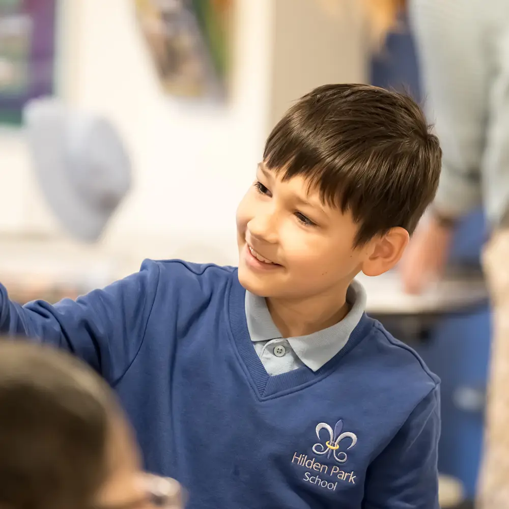 A young boy at Hilden Park School with black hair wearing the school uniform pointing at something
