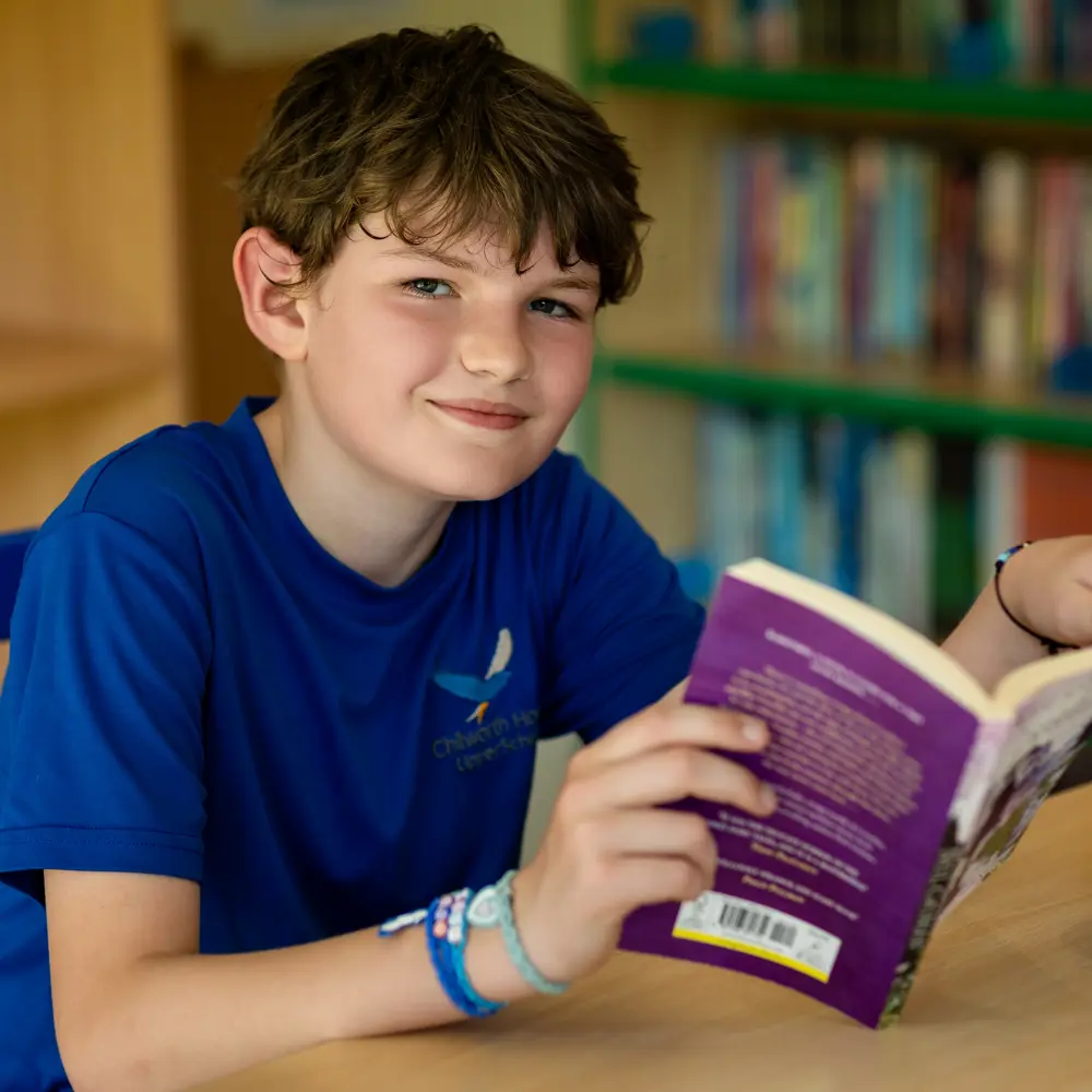 A young boy with brown hair at Chilworth House Upper School reading a book at a desk