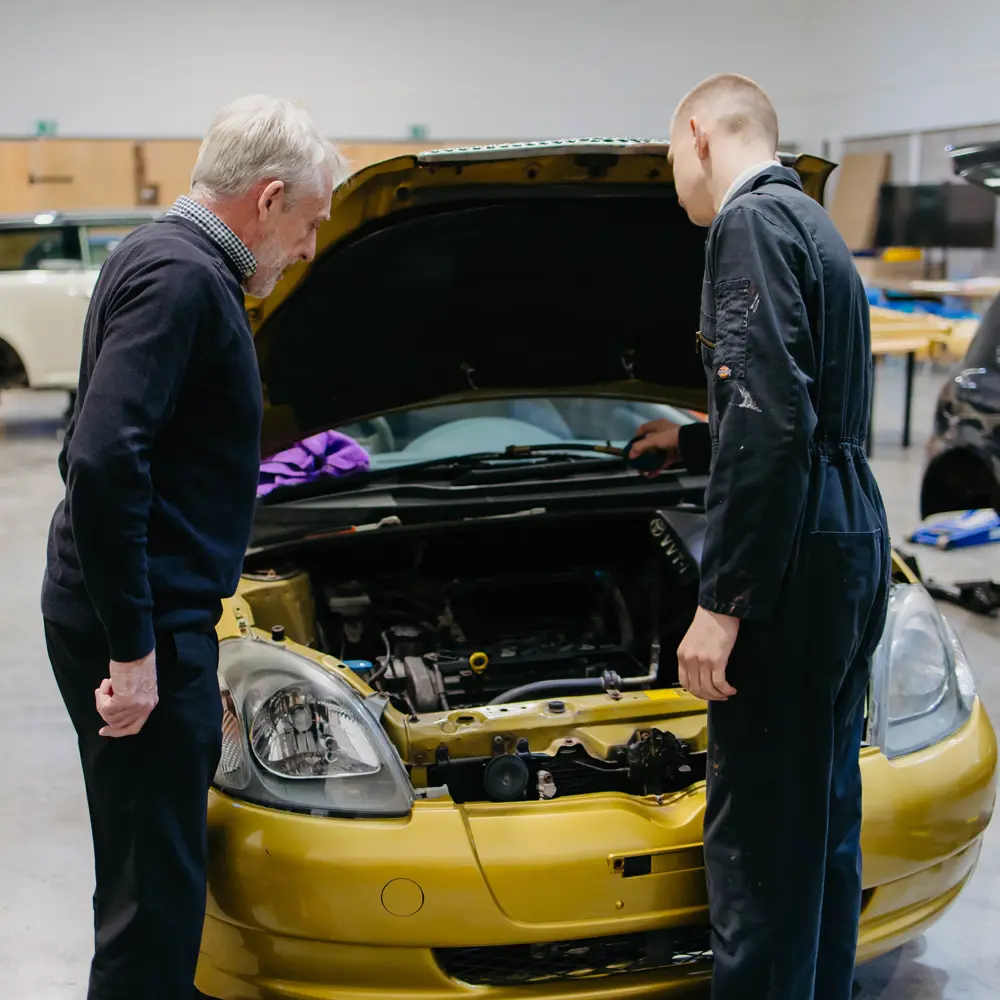 Male pupil and male member of staff in Cumberland School's car workshop looking under the bonnet of a car