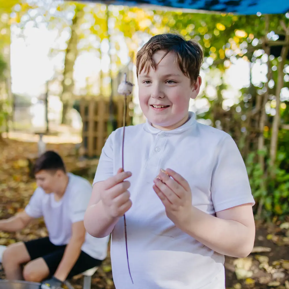 Brown-haired boy staring at a burnt marshmallow on a stick by a campfire