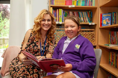 A woman and a girl smile while reading a book together in the library at Lakeside School.
