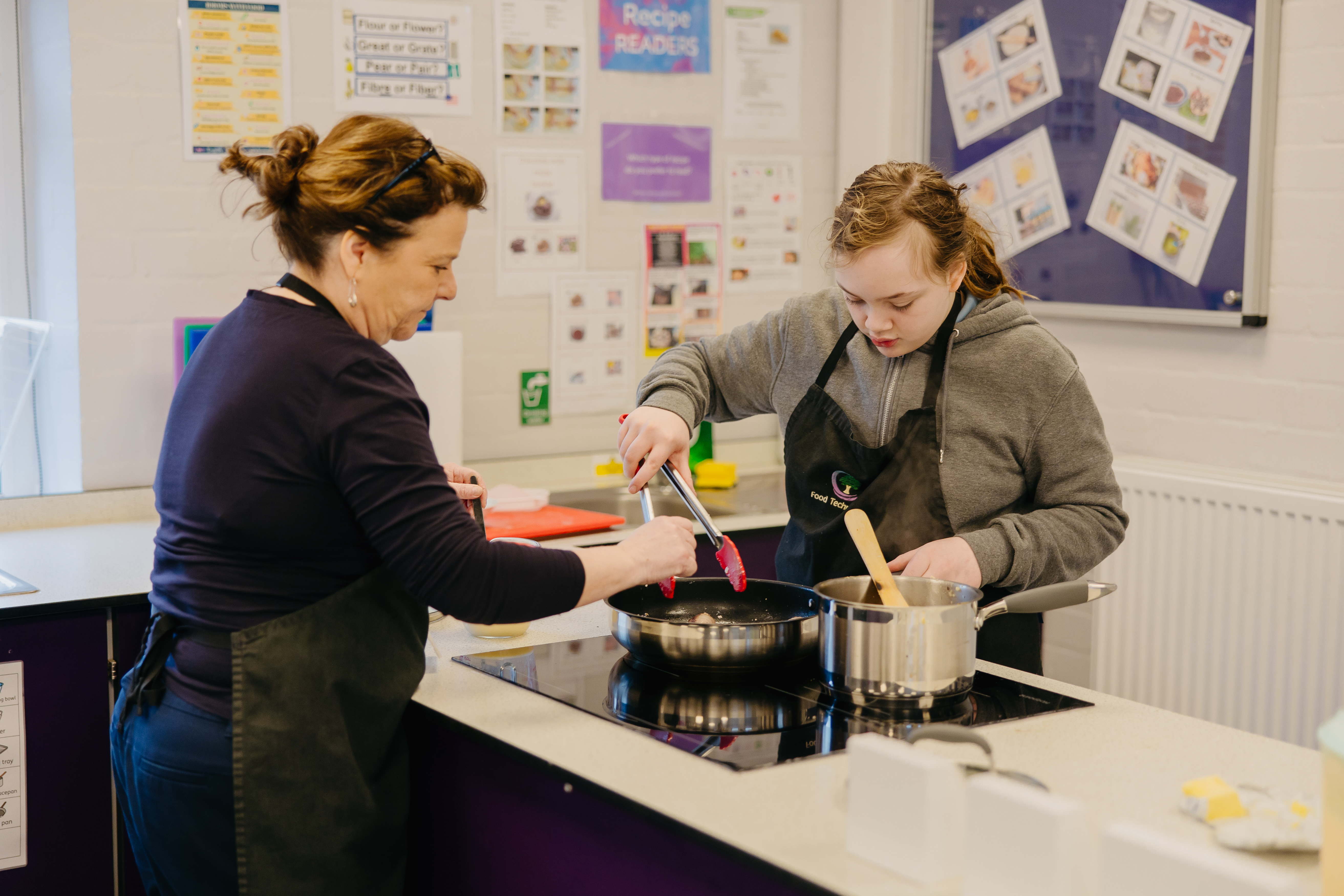 Teacher helping girl to stir food on hob in cooking class