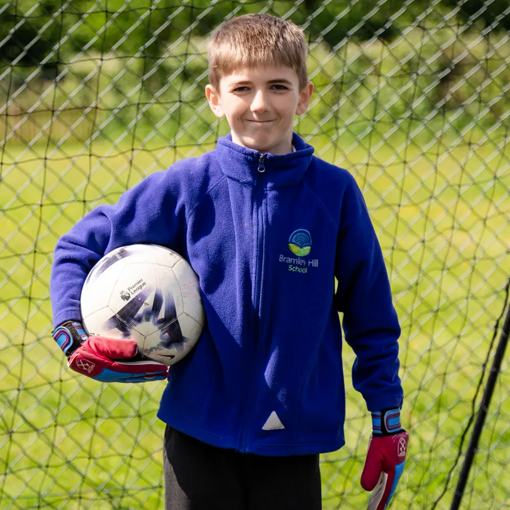 Young boy from Bramley Hill School stood in a football net holding a football with gloves on