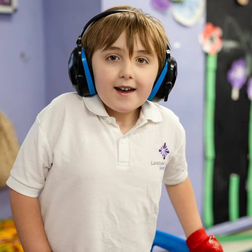 A young boy at Lavender Lodge School smiling at the camera wearing ear defenders
