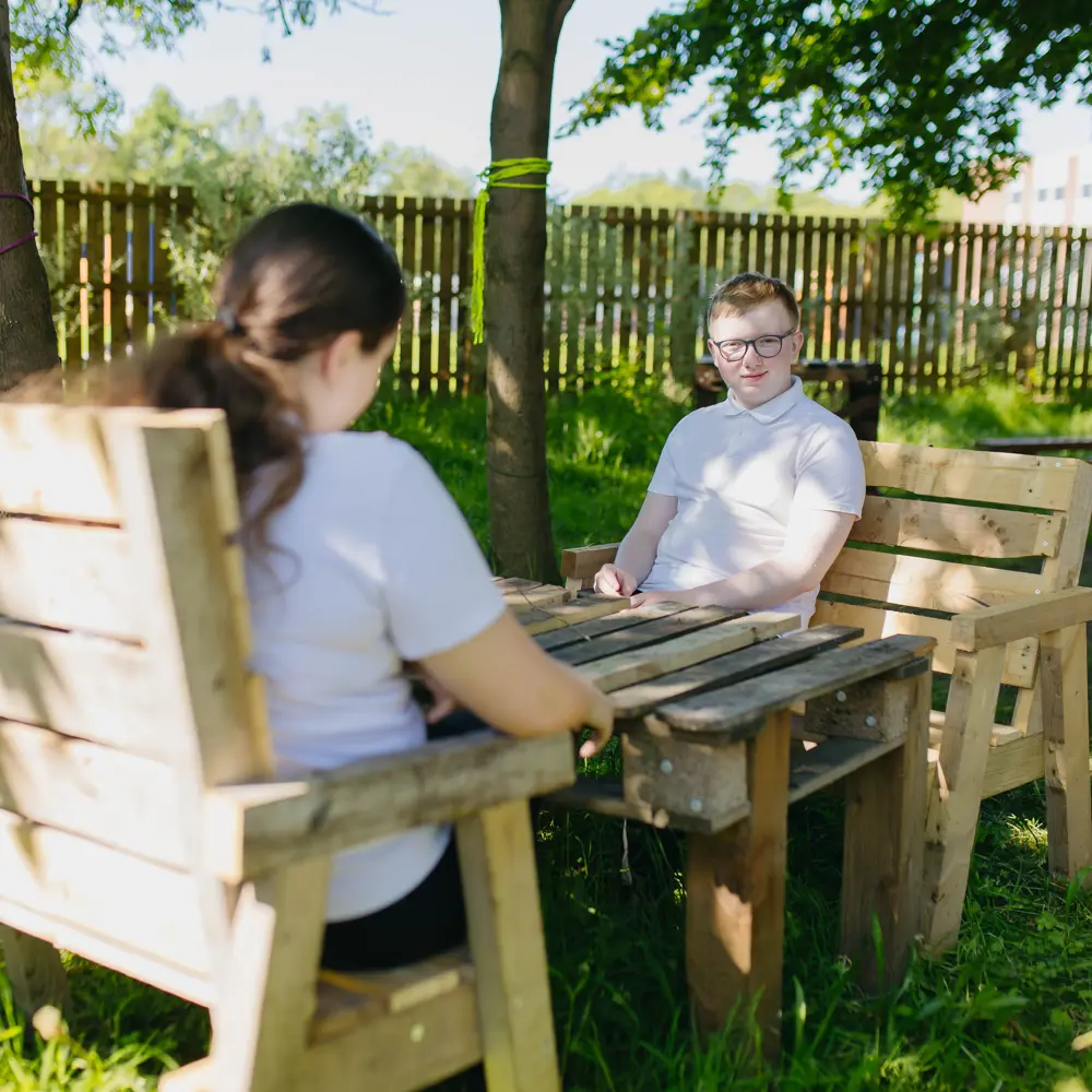 Two pupils at Hartwell School say on a bench outside under the trees
