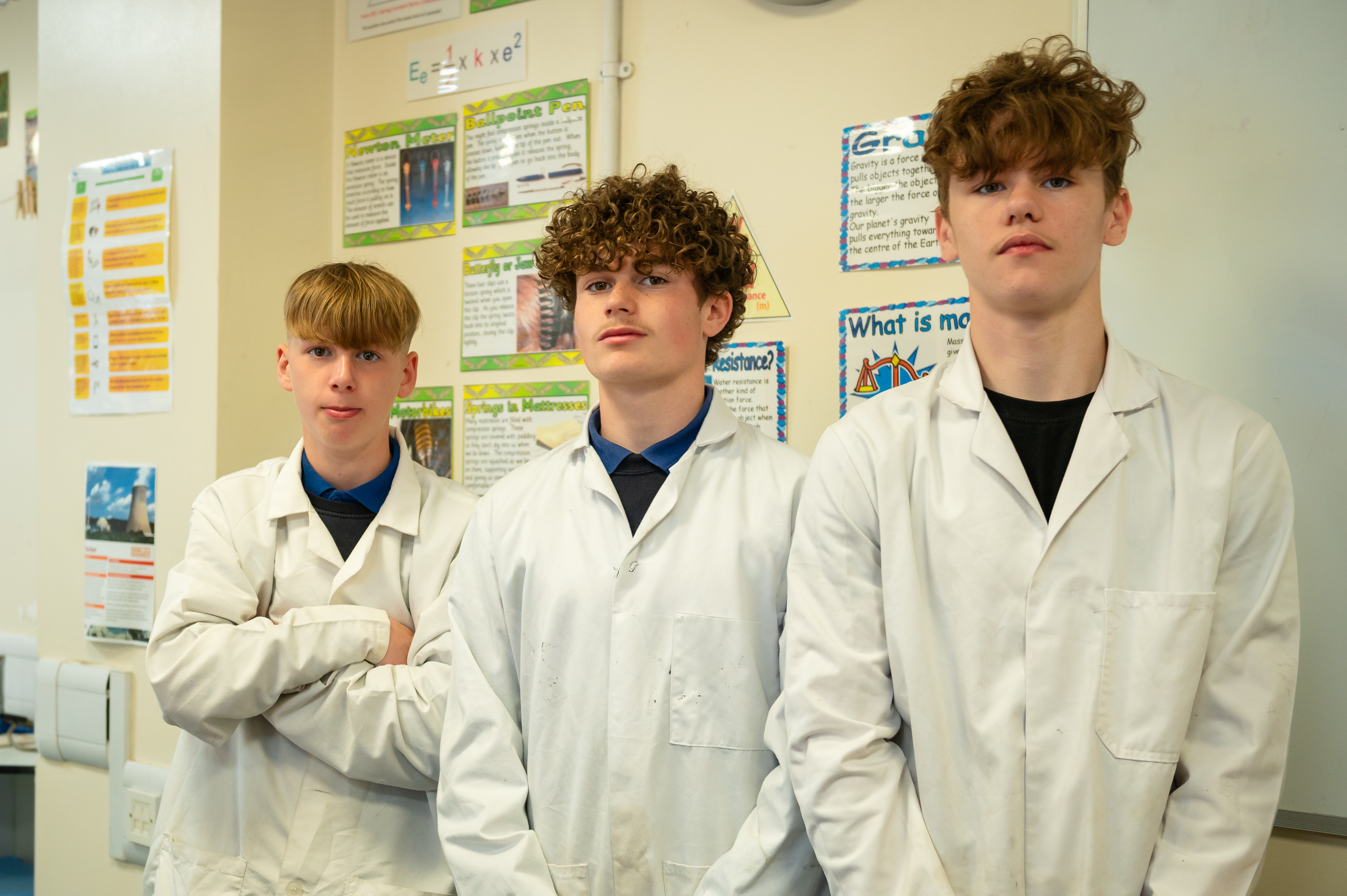 Three older pupils wearing lab coats stood in a row and looking at camera