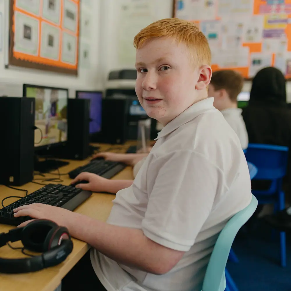 A young boy in a white polo shirt in a classroom on a computer
