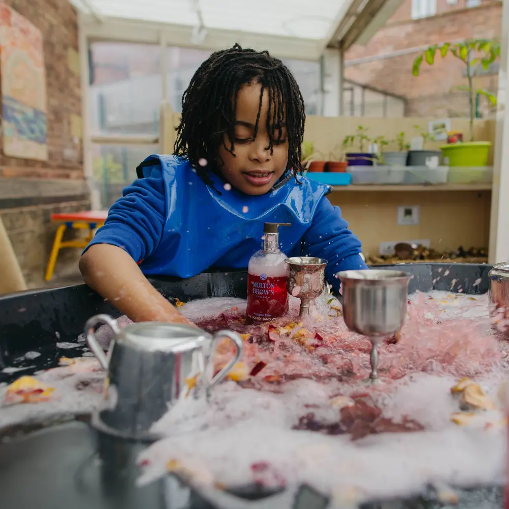 Young boy at Westmorland School smiling playing with a sensory tray
